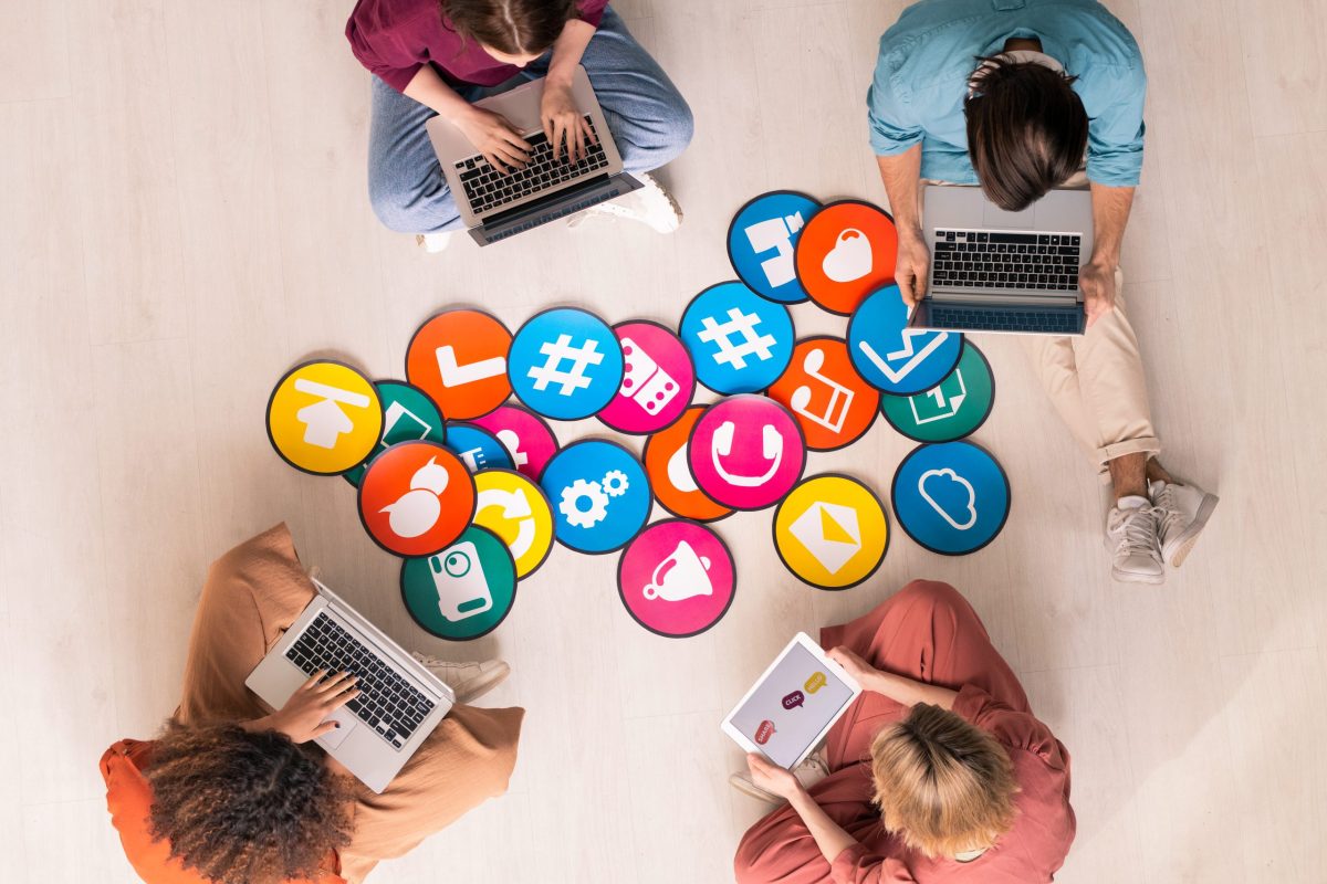 Young friendly people in casualwear sitting by multi-color papers with icons Choosing the Right Social Media Partner